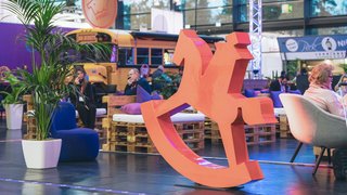 Großes rotes Schaukelpferd-Logo, Sitzbereich mit Palettenmöbeln und gelbem Bus im Hintergrund.