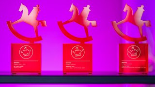 Drei rote ToyAward-Trophäen vor violettem Hintergrund.