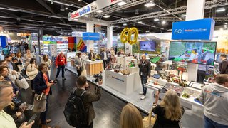 Fischertechnik booth with 60-year balloon, visitors and cameras, many models on display.