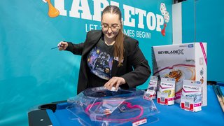 Person demonstriert Beyblade-Spiel an einem Stand.