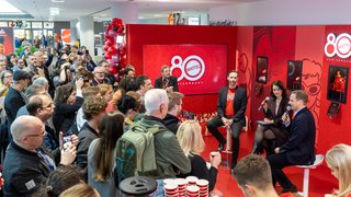 Press event with audience at red Mattel 80 years stage, interview with microphones.